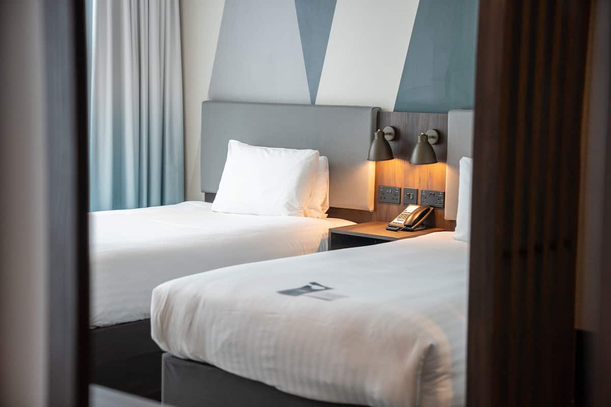 Una habitación de hotel con dos camas, una mesita de noche con lámpara y un teléfono.