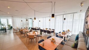 A modern dining area with round tables, chairs, and a sofa. - Holiday Inn London - Whitechapel by IHG (London)