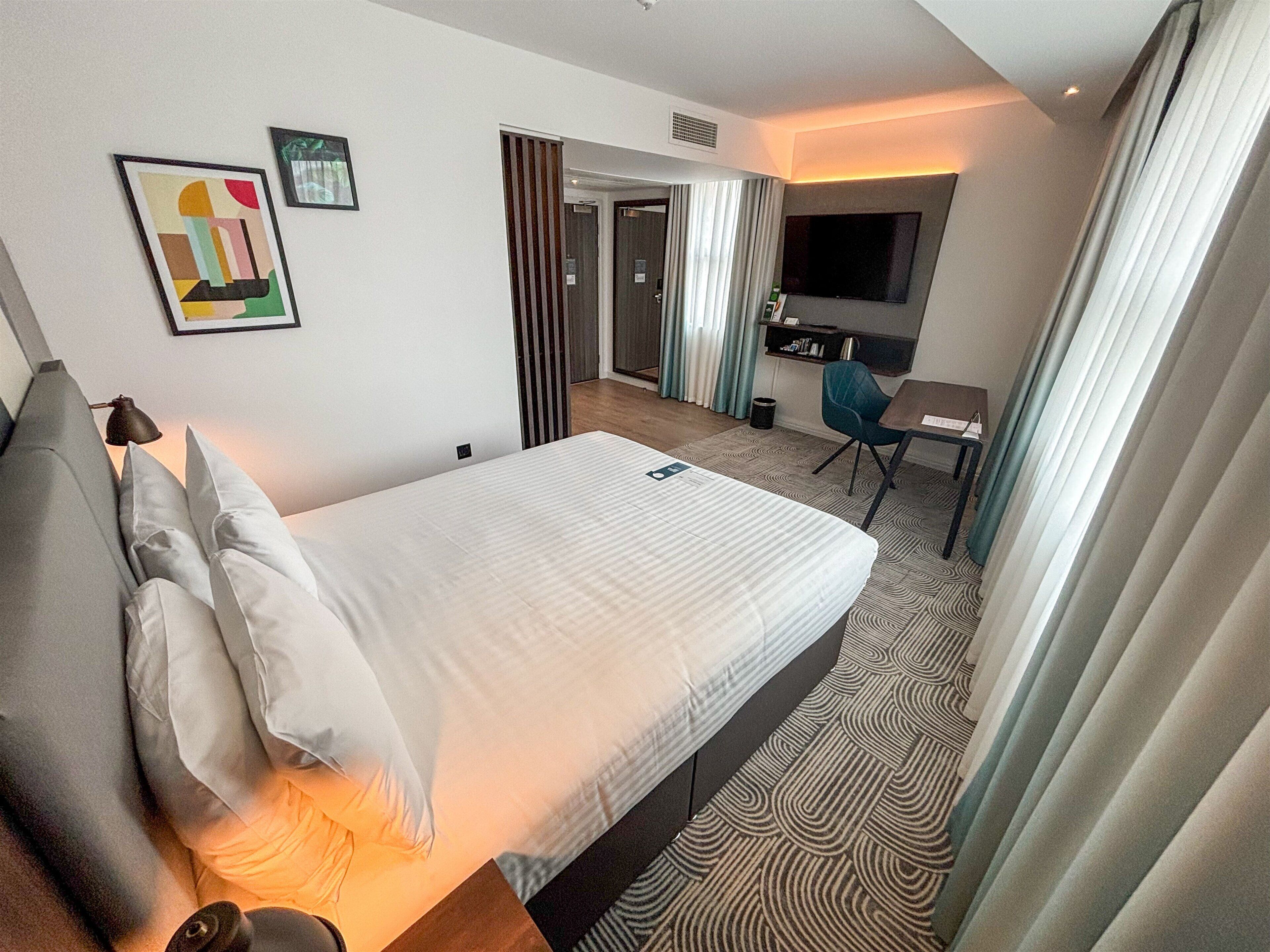 Une chambre d’hôtel équipée d’un lit, d’un bureau, d’une chaise, d’une télévision et d’une porte donnant accès à une salle de bain.