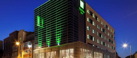 A modern hotel building with a prominent Holiday Inn sign, multiple floors, and a glass facade.