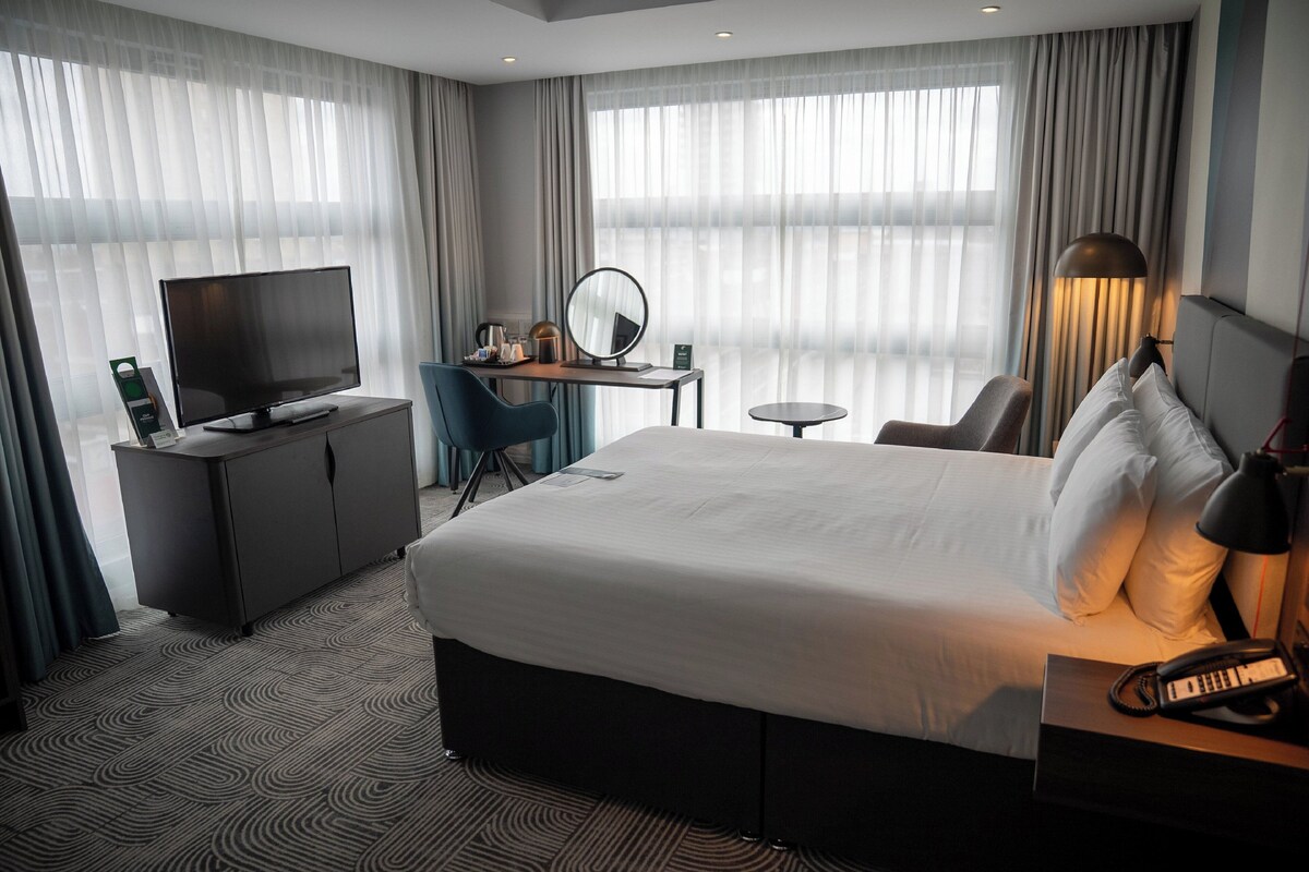 A hotel room with a large bed, a desk with a computer, a television, and a chair.
