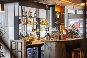 Un espace bar avec des étagères remplies de bouteilles et de verres, un réfrigérateur et une machine à café.