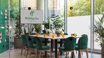 A Holiday Inn hotel conference room with a large table, green chairs, and potted plants.