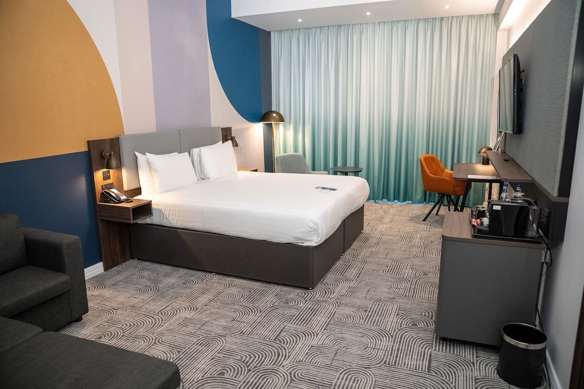 A modern hotel room with a large bed, a desk, a chair, and a TV.