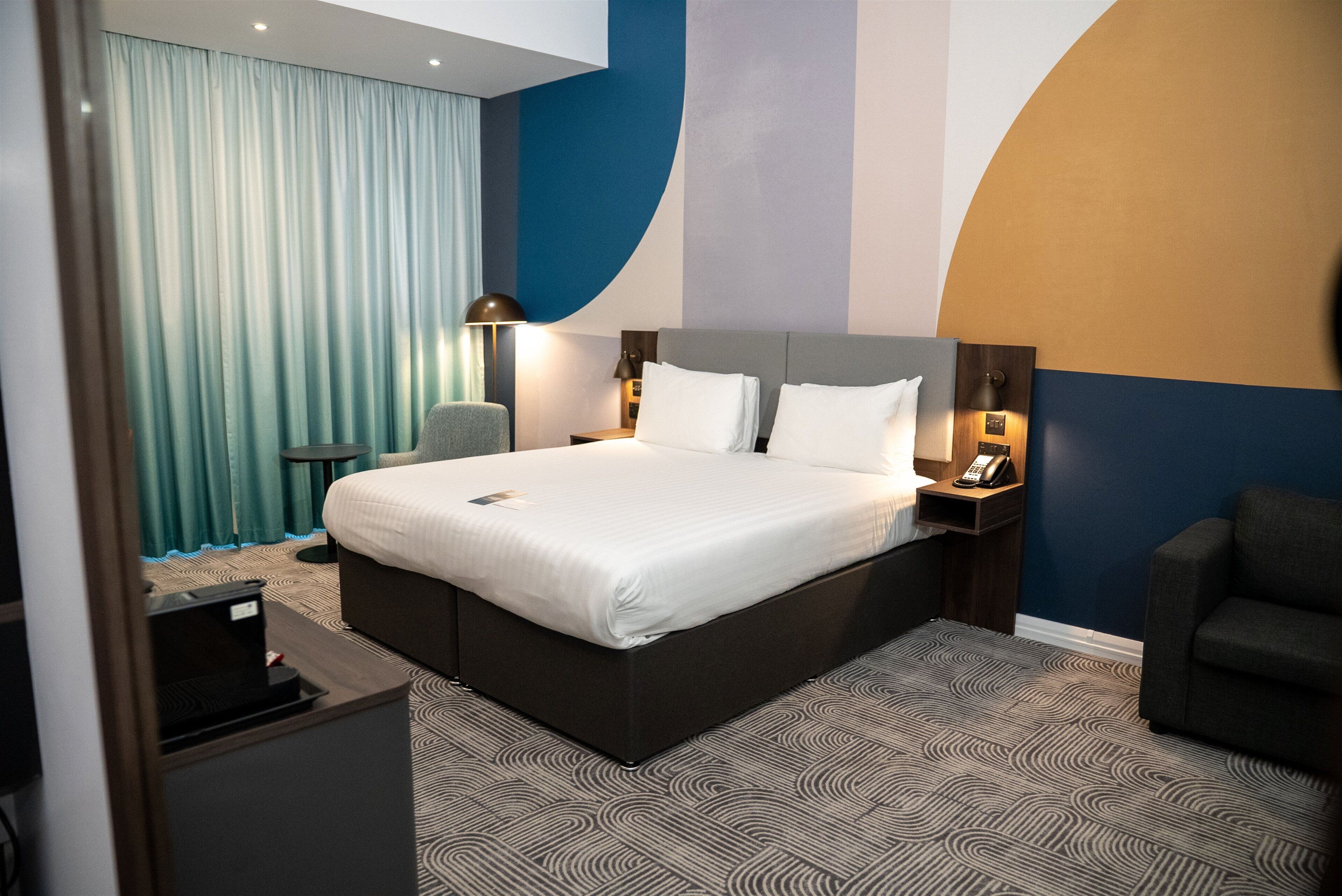 Une chambre d’hôtel avec un grand lit, des tables de chevet avec des lampes, une chaise et un bureau avec un ordinateur.
