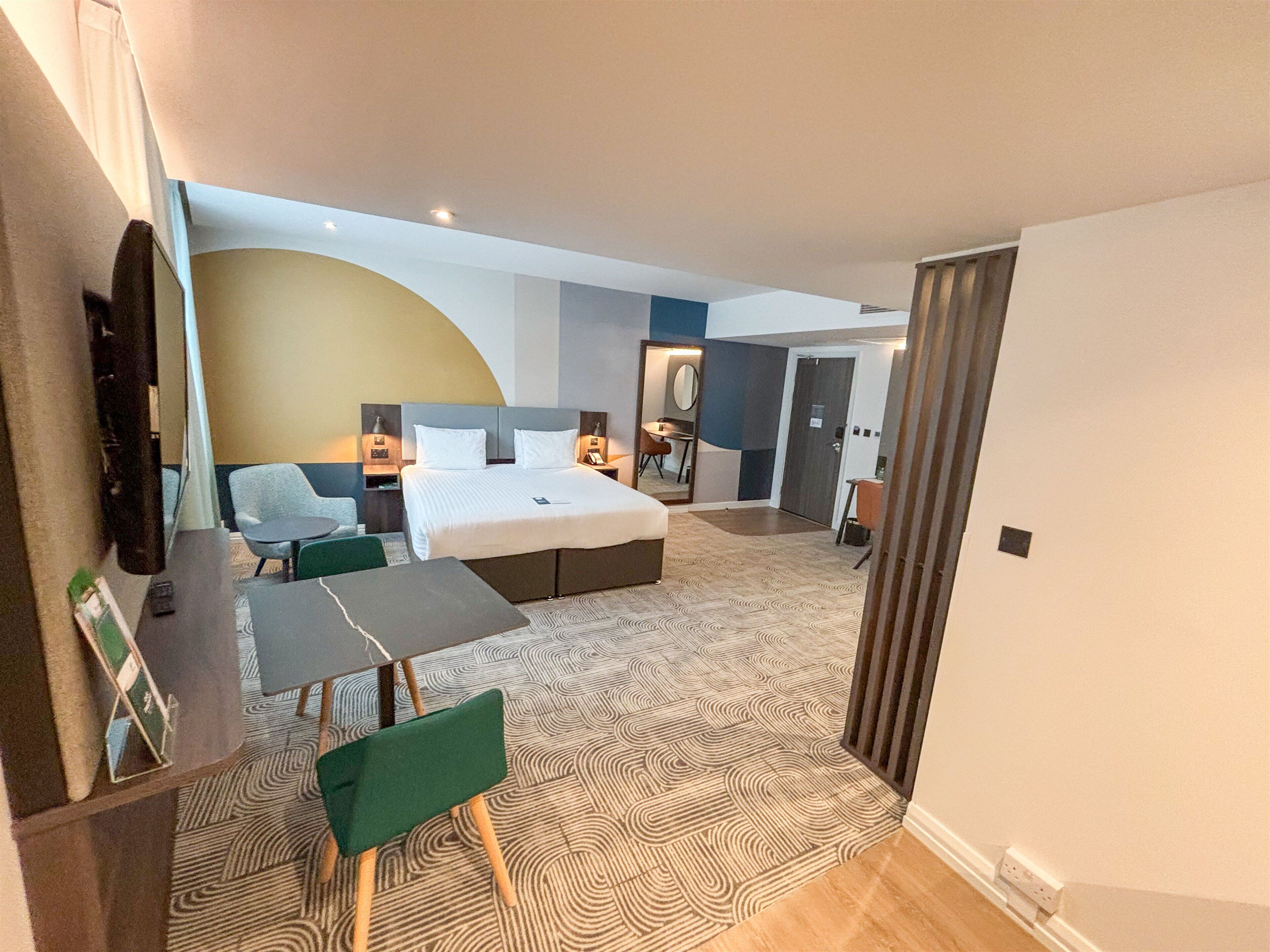 A hotel room with a bed, a desk, a chair, a TV, and a bathroom.