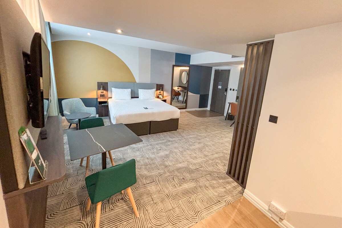 A hotel room with a bed, a desk, a chair, a TV, and a bathroom.