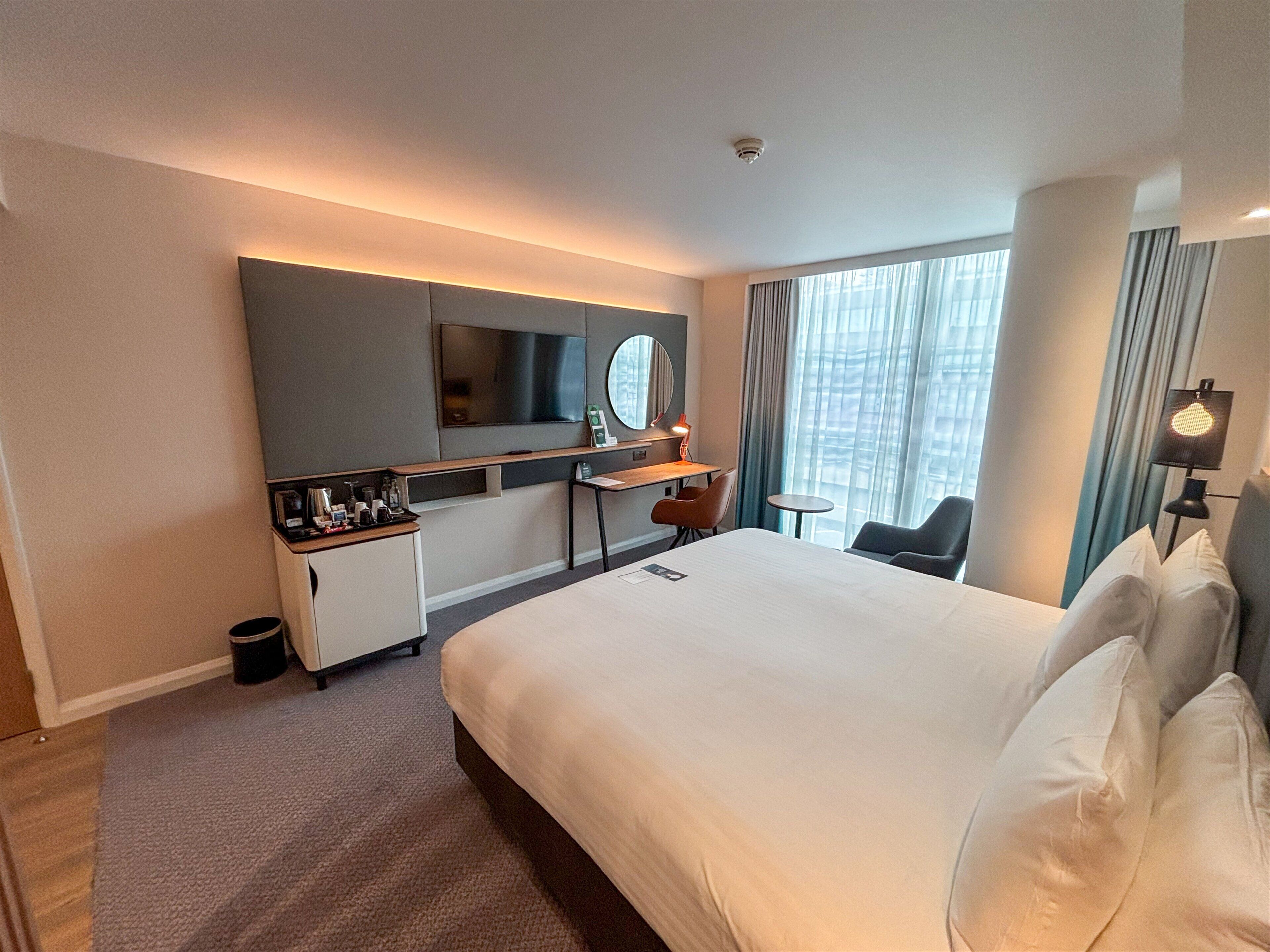 A hotel room with a bed, a desk, a chair, a TV, and a window with curtains.
