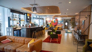 A modern bar area with a variety of liquor bottles, a seating area with a sofa and chairs, and a mural on the wall. - Holiday Inn London - Whitechapel by IHG (London)