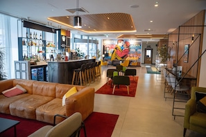 A modern bar area with a variety of liquor bottles, a seating area with a sofa and chairs, and a mural on the wall. - Holiday Inn London - Whitechapel by IHG (London)