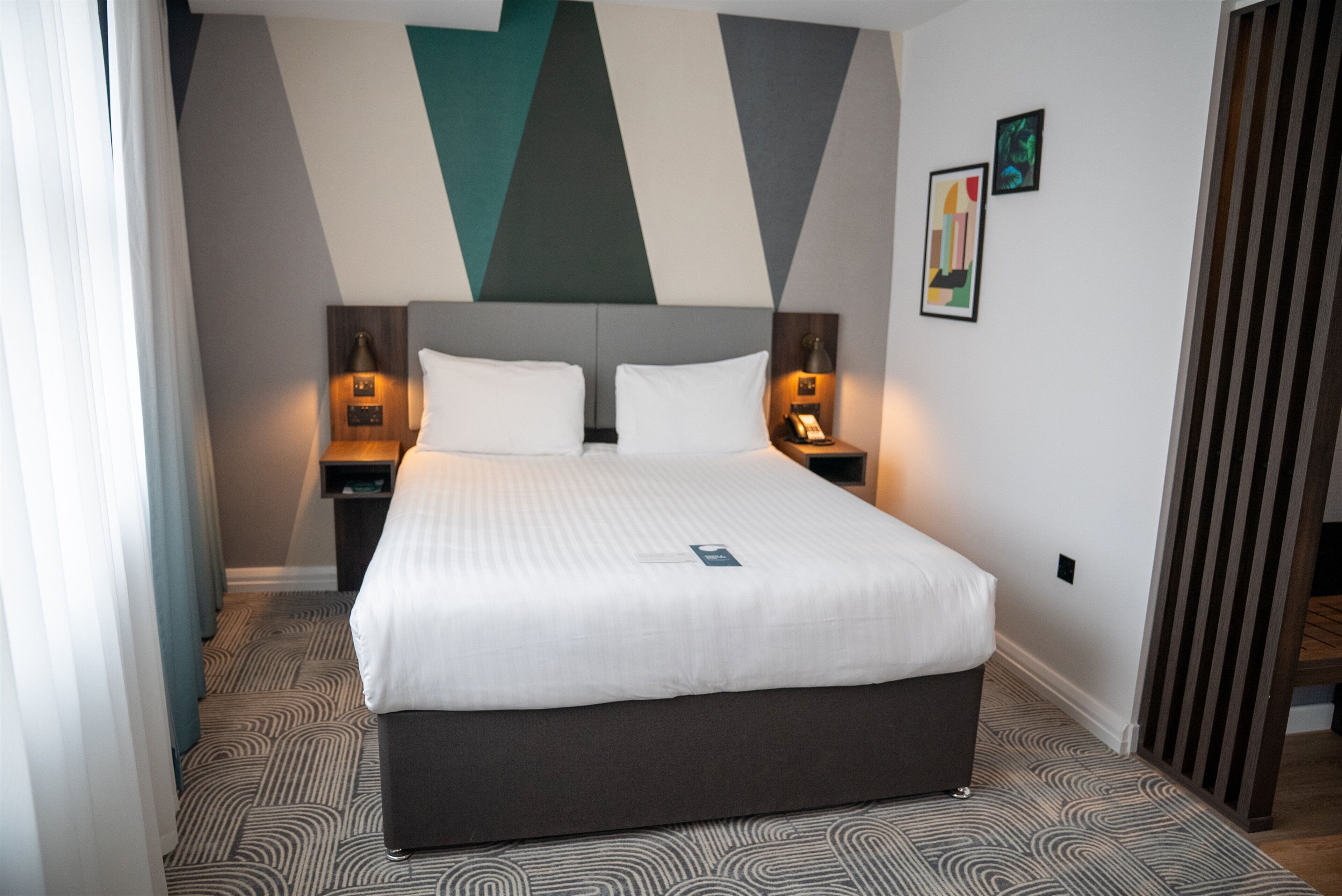 A hotel room with a large bed, two bedside tables with lamps, a headboard, and a patterned carpet.