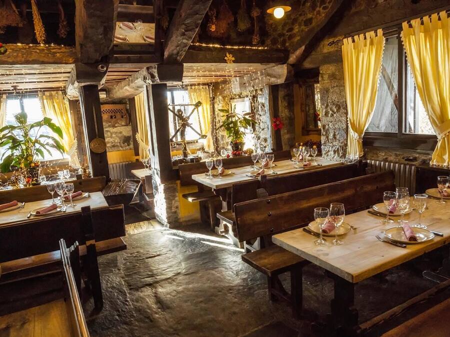A rustic restaurant with wooden tables and benches, stone walls, and hanging plants.