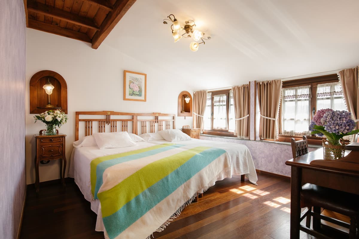 Ein Schlafzimmer mit einem großen Bett, einem Holzkopfstück, einem Nachttisch mit Lampe, einem Fenster mit Vorhängen und einer Kandelaber.