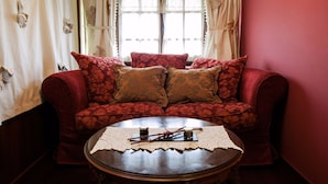 Una sala de estar acogedora con un sofá rojo, dos almohadas a juego y una mesa de centro de madera con un mantel de encaje.