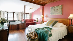 Una habitación con techo de madera, una cama con manta verde y blanca, un sofá rojo, una mesita con una lámpara y un ventanal con cortinas.