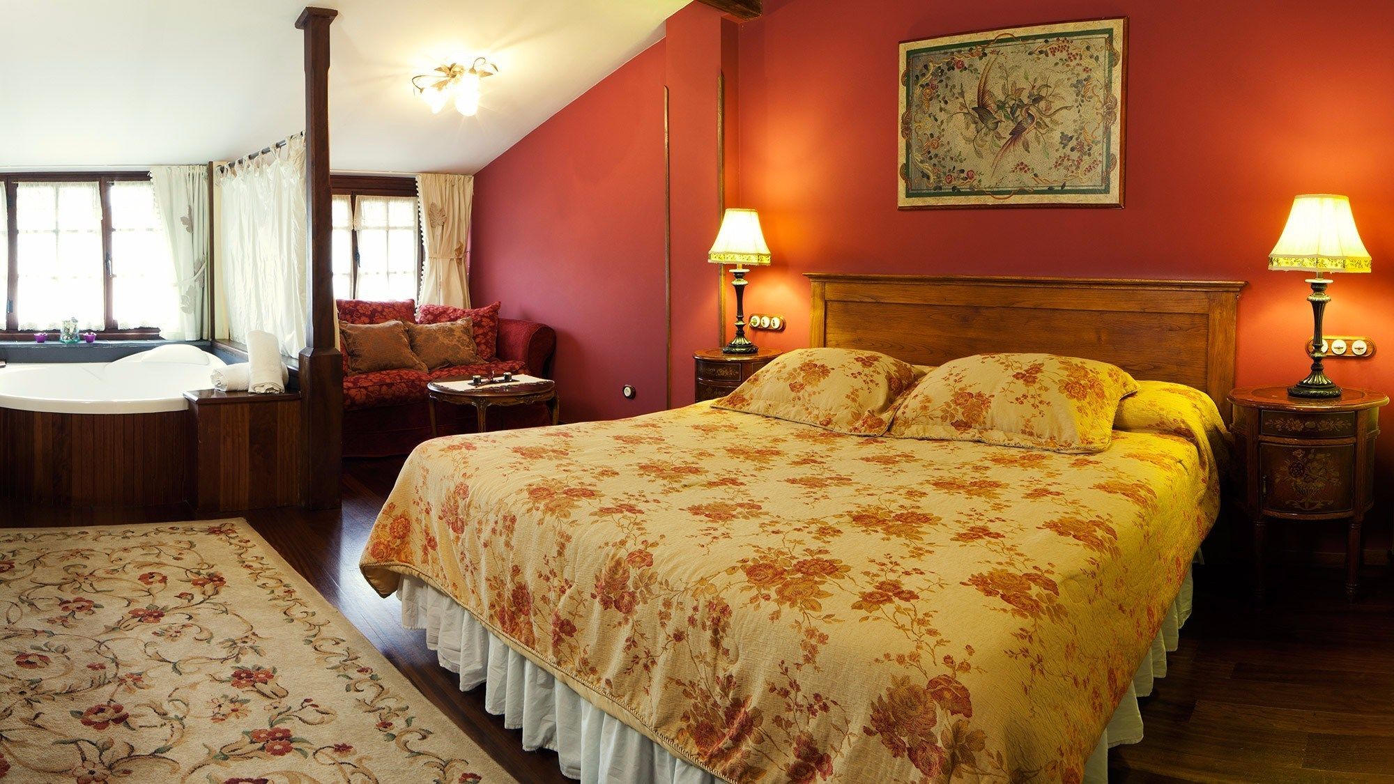 A bedroom with a large bed, a sitting area with a sofa, a bathtub, and a wooden headboard.