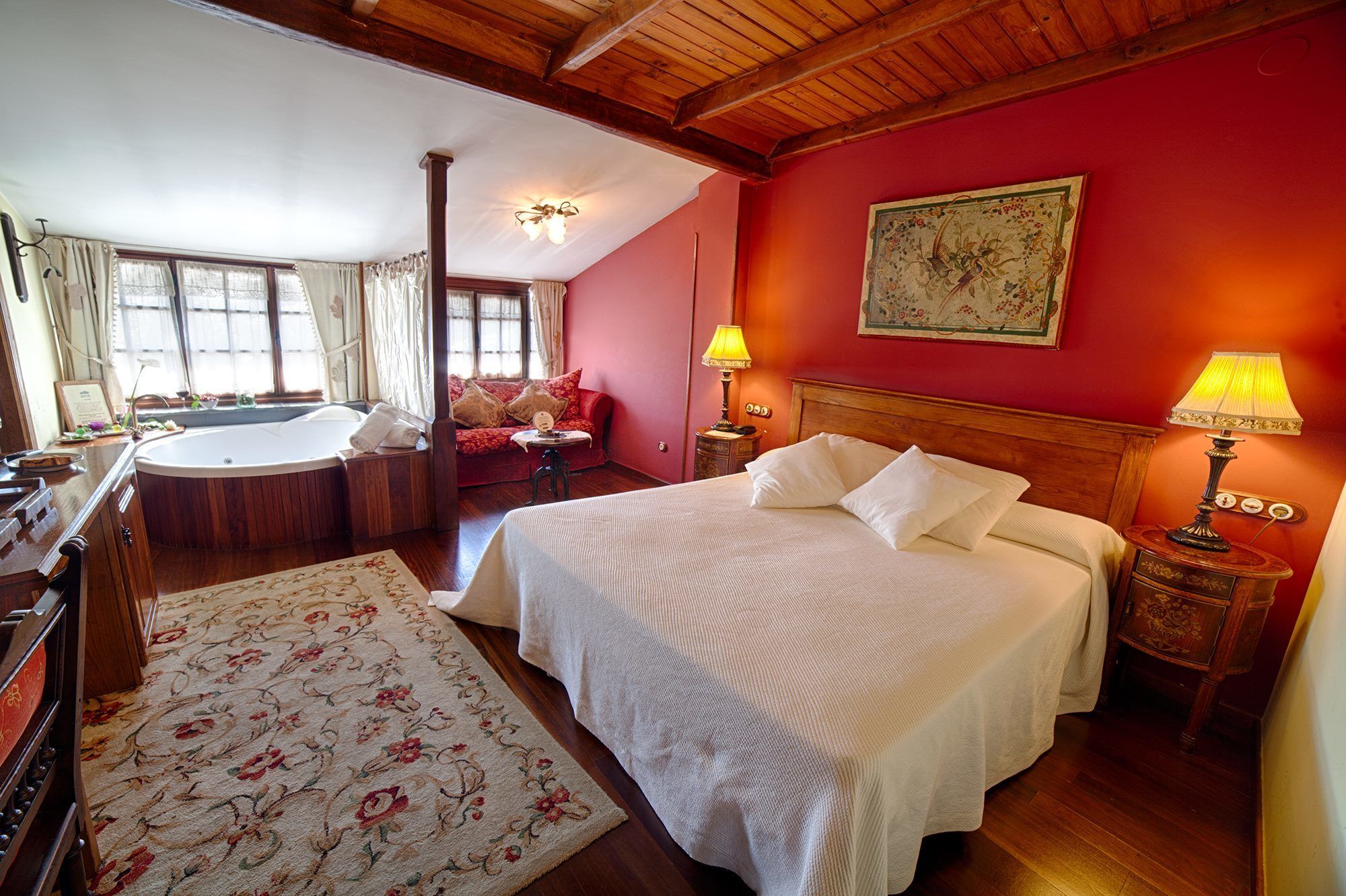 Un dormitorio con una cama grande, una zona de estar con sofá, una bañera y techo de madera.