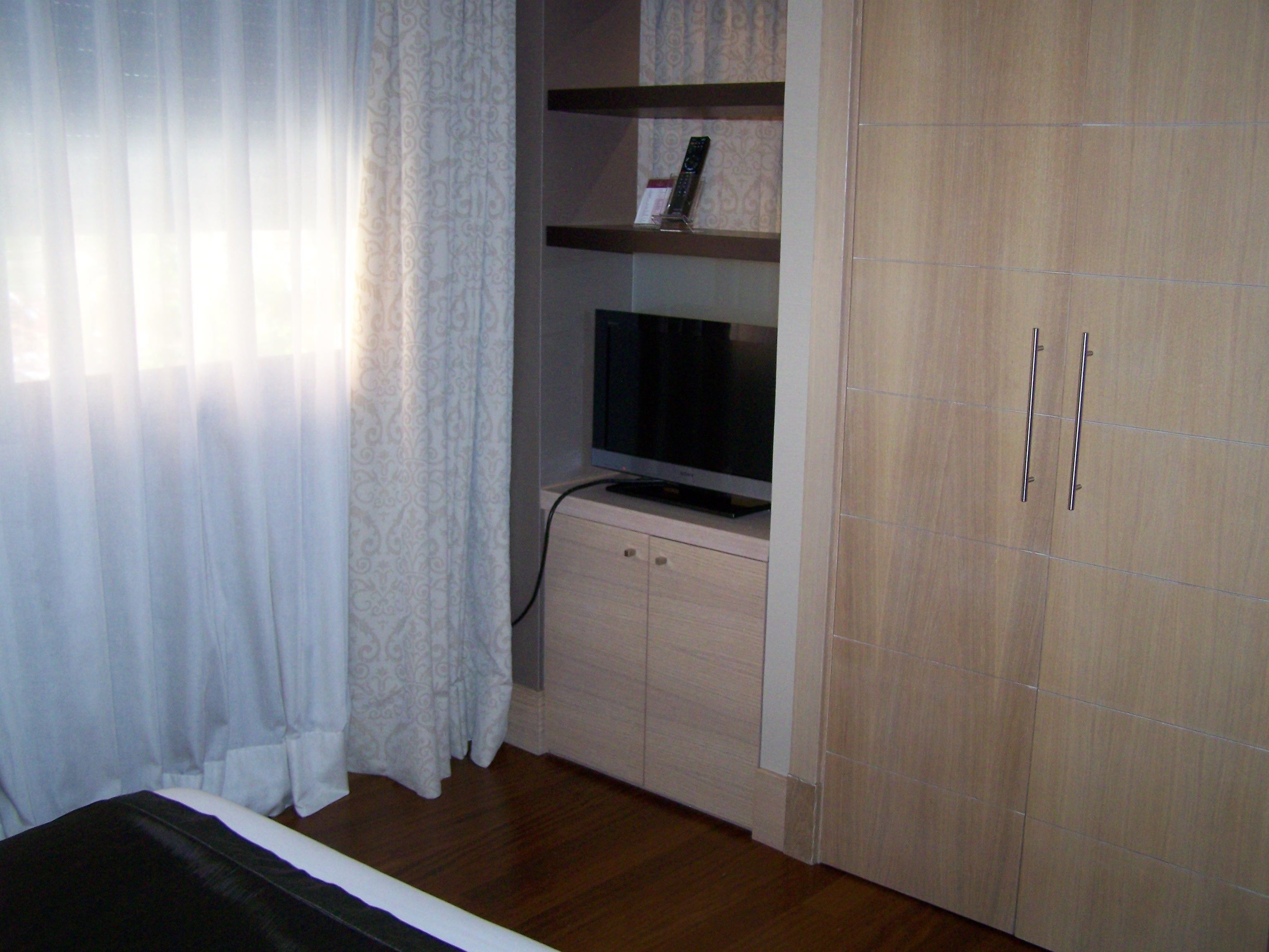 A bedroom with a bed, a TV on a stand, a wardrobe, and a curtain.