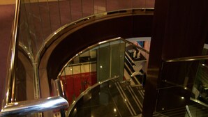 Una escalera de cristal curva con barandillas de metal, que desciende a un nivel inferior.