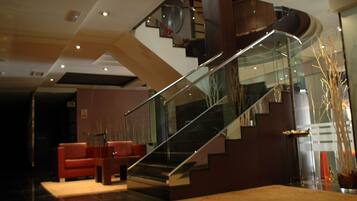Un interior moderno con una escalera de cristal, un sofá rojo y un jarrón con ramas.