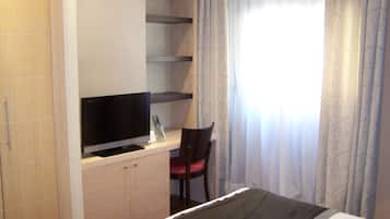 Hotelkamer met een bed, een televisie op een houten kast, een bureau met stoel en een raam met gordijnen.