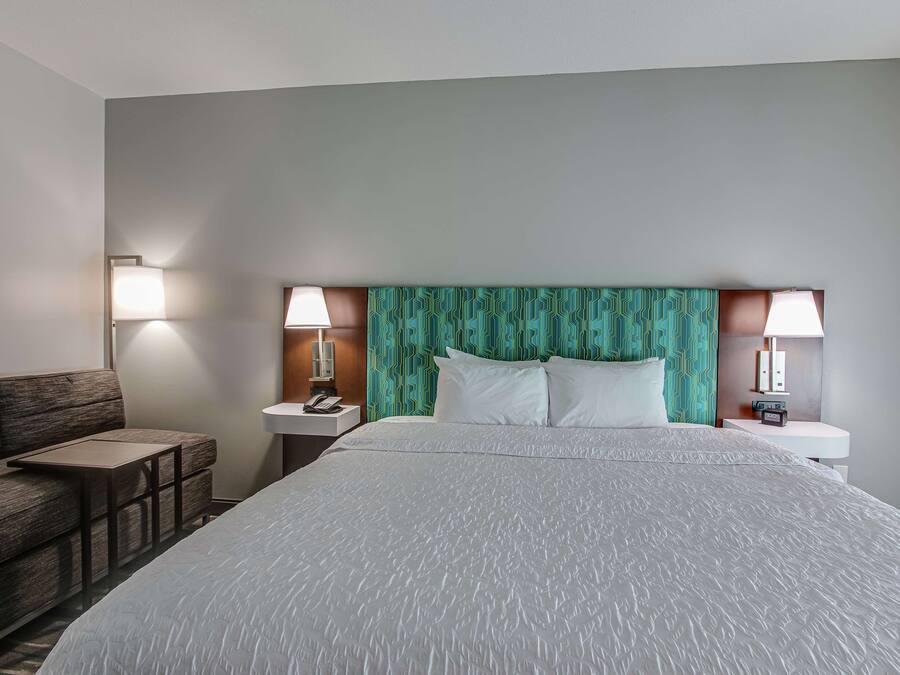 Habitación de hotel con una cama grande, un sofá, dos mesitas de noche con lámparas y un cabecero estampado.