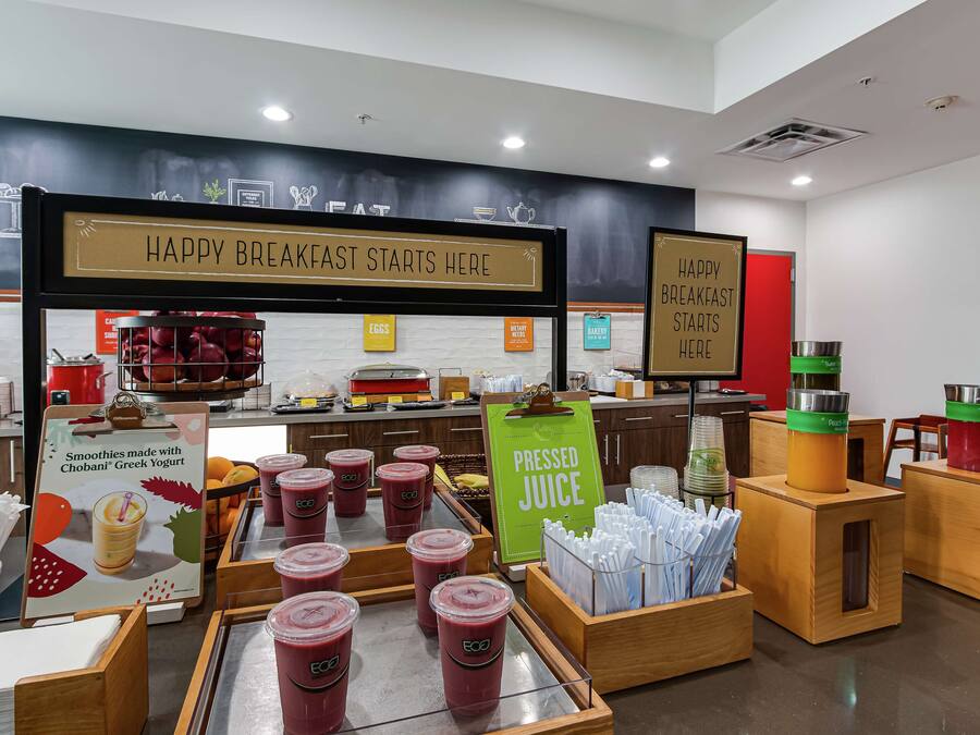 Un coin petit-déjeuner agrémenté d’une pancarte sur laquelle on peut lire « UN BON PETIT-DÉJEUNER COMMENCE ICI » et où sont présentés des smoothies et des jus de fruits fraîchement pressés.