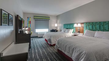 Quarto de hotel com duas camas, uma escrivaninha, uma cadeira, um abajur e uma janela com persianas.