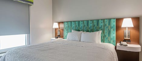 Una habitación de hotel con una cama grande, dos mesitas de noche con lámparas, un cabecero con estampado geométrico y una ventana con persianas.