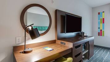 Quarto de hotel moderno com escrivaninha de madeira, espelho redondo, TV de tela plana e decoração colorida na parede.