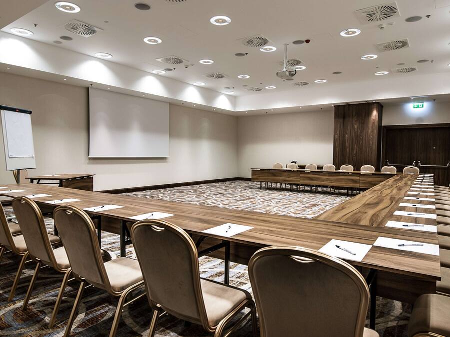 A conference room with a long table, chairs, a projector screen, and a carpeted floor.
