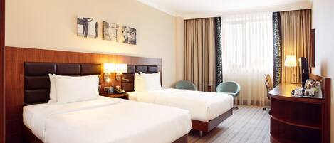 A hotel room with two beds, a desk, a chair, and a large window with curtains.