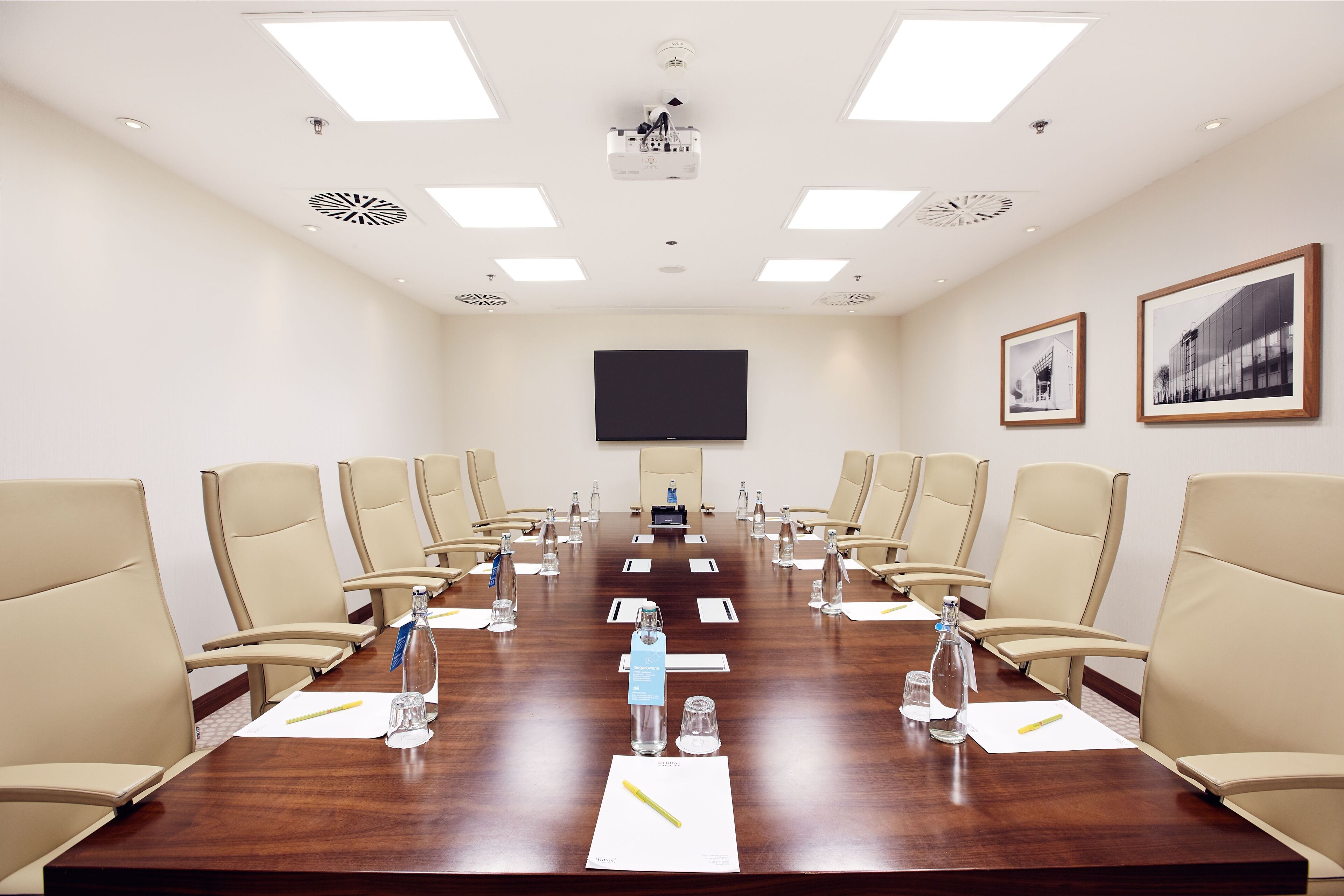 Une salle de conférence avec une longue table, des chaises de couleur beige, des bouteilles d’eau et un écran de projection.