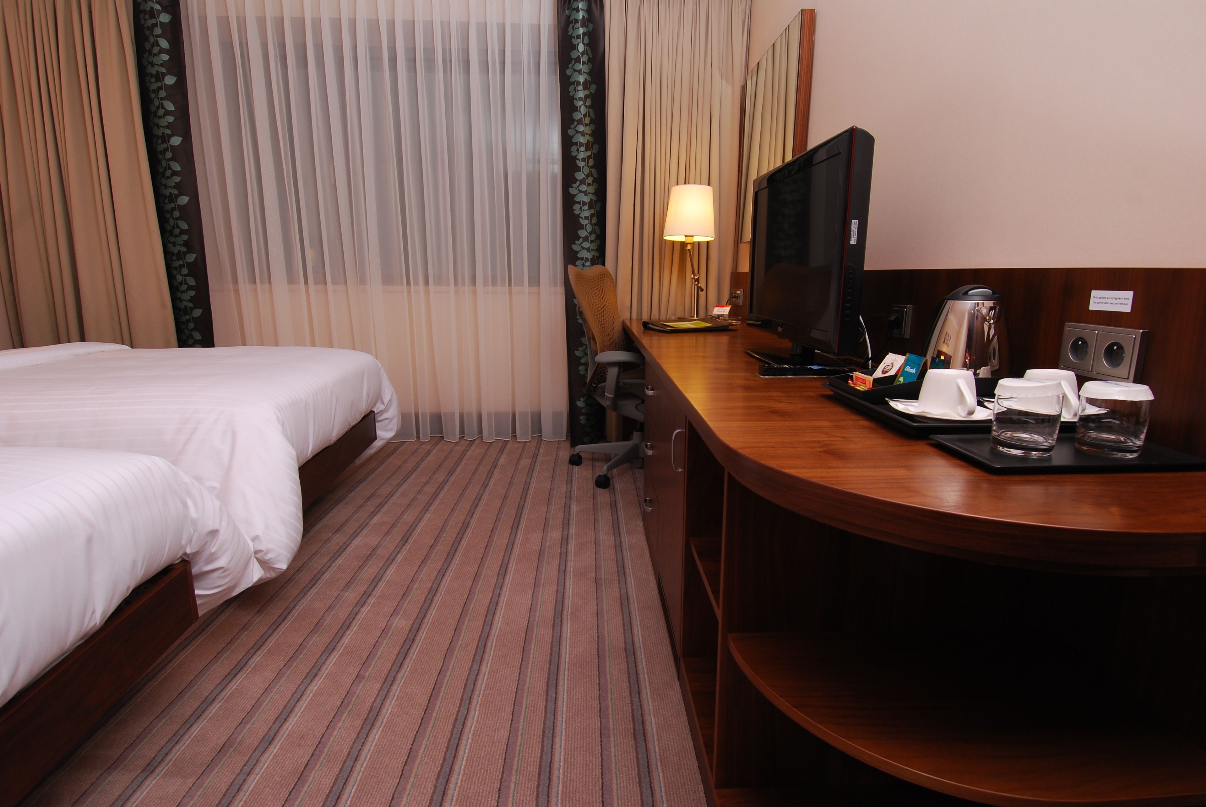 A hotel room with a bed, a desk with a television, a coffee maker, and a lamp.