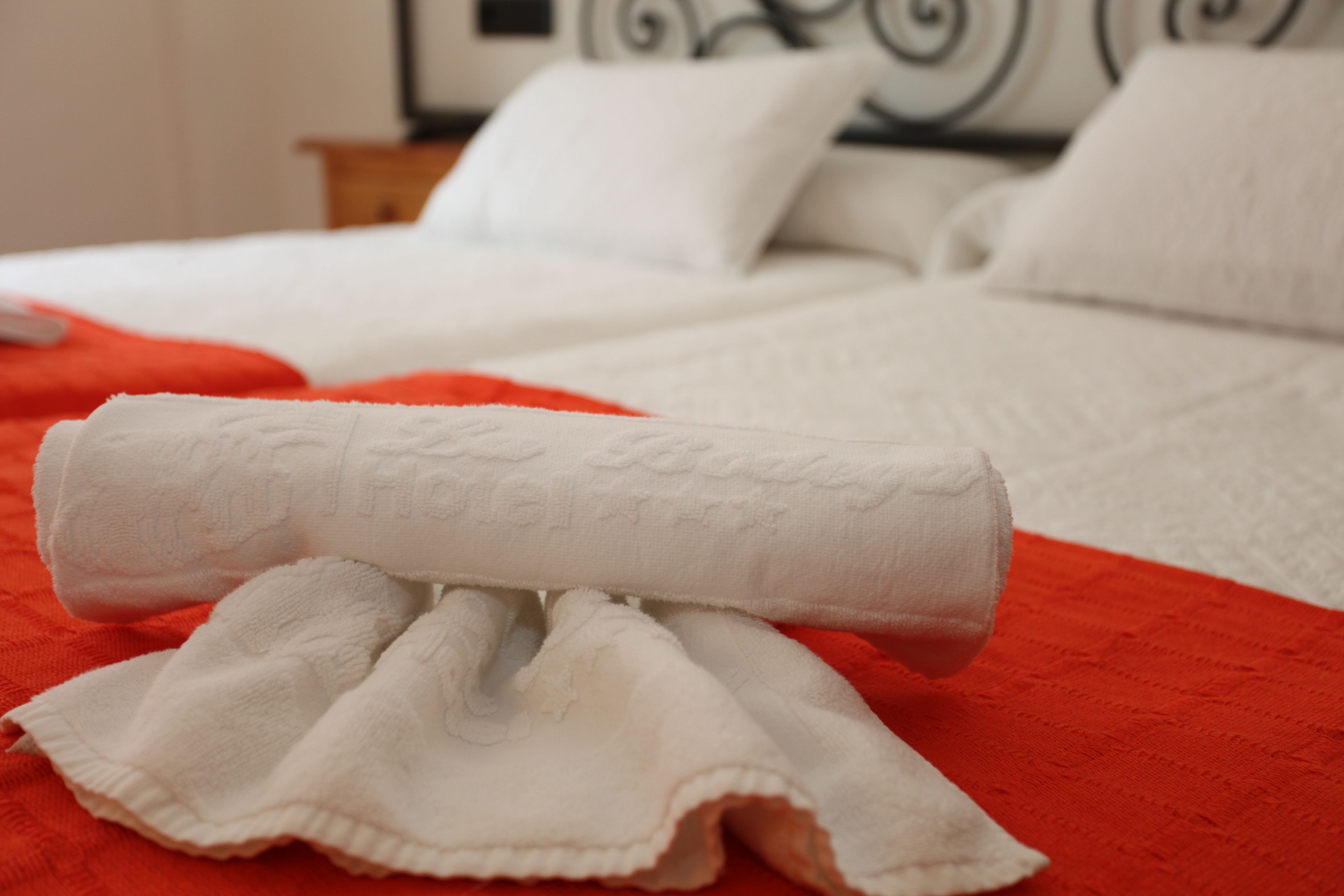 Una cama bien tendida con sábanas blancas y una colcha roja.