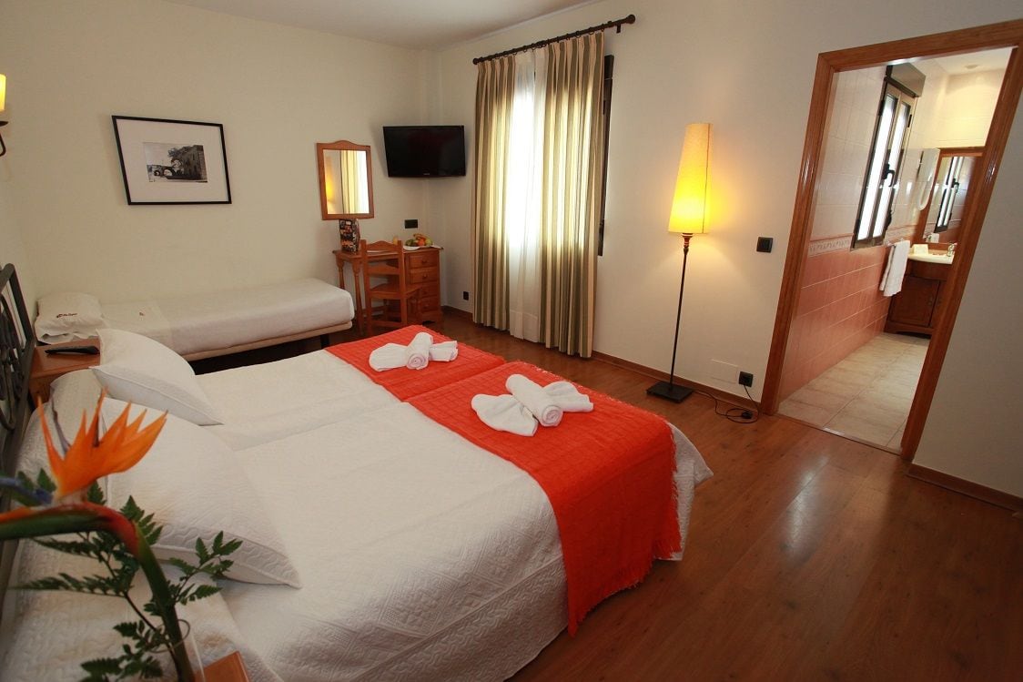 Habitación de hotel con cama, escritorio, silla, televisión y baño visible a través de una puerta abierta.