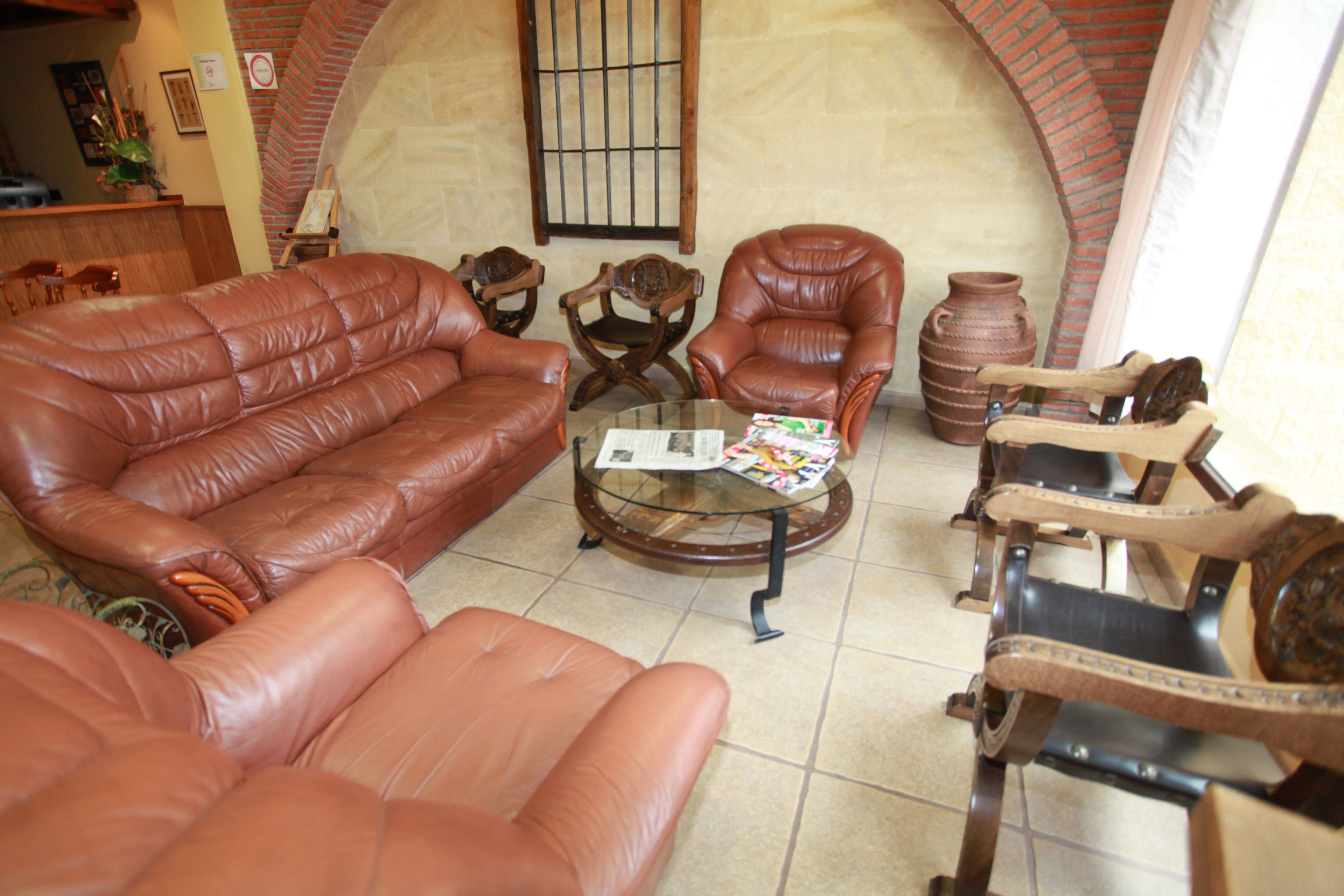 A living room with a leather sofa, two armchairs, a coffee table with magazines, and a brick fireplace.