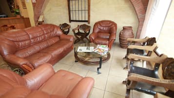 A living room with a leather sofa, two armchairs, a coffee table with magazines, and a brick fireplace.