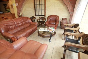 A living room with a leather sofa, two armchairs, a coffee table with magazines, and a brick fireplace. - La Bodega Hotel (Ciudad Rodrigo)