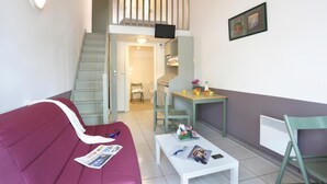 A compact living space with a staircase leading to an upper level, a dining area, and a seating area with a sofa and coffee table.