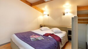 A bedroom with a skylight, two bedside lamps, a bed with a purple blanket, and a magazine on the bed.