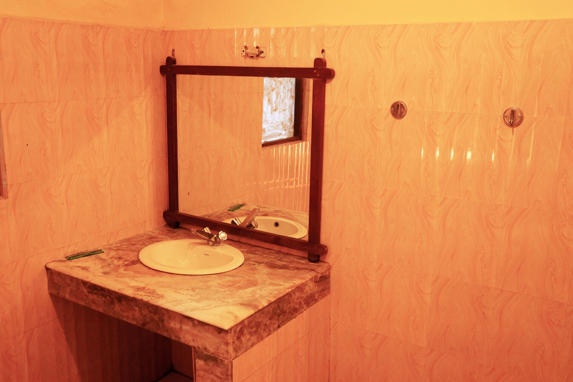 A bathroom with a marble sink, a wooden-framed mirror, and a wooden wall.