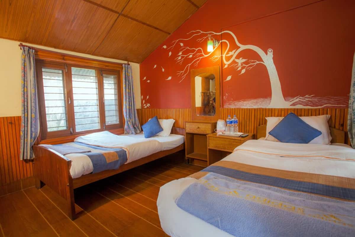 A room with two single beds, wooden flooring, a wooden ceiling, a wall mural, a mirror, and a desk with a chair.