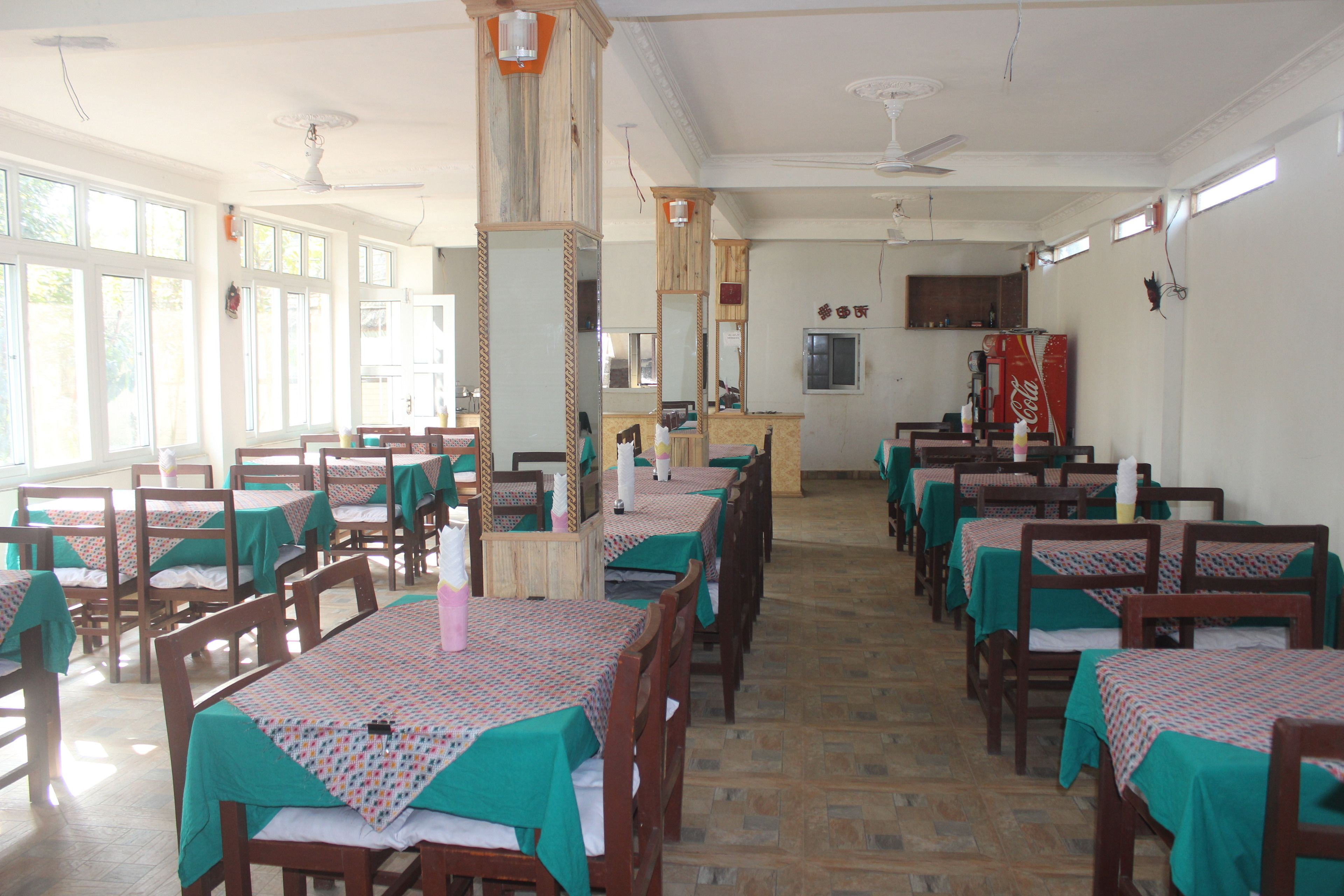 A dining area with multiple tables and chairs, wooden floors, and large windows allowing natural light.