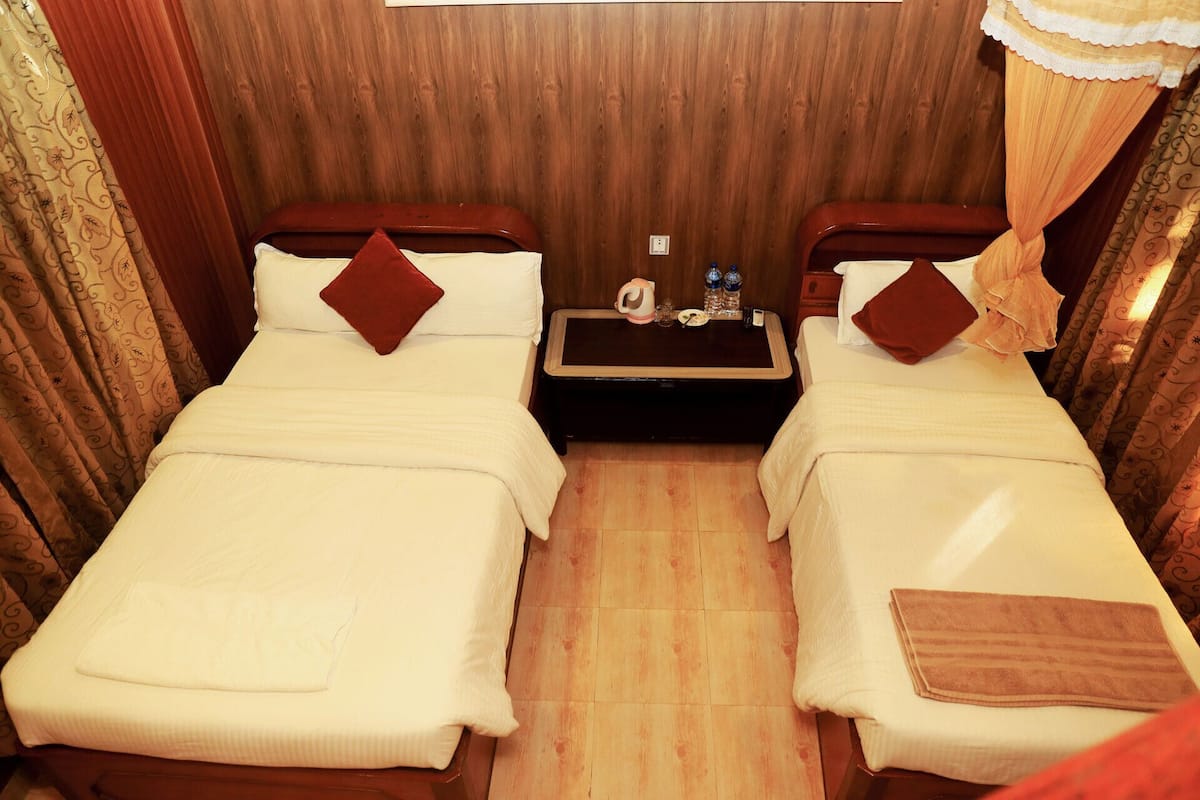 A hotel room with two beds, a small table with a kettle and bottles, and a wooden floor.