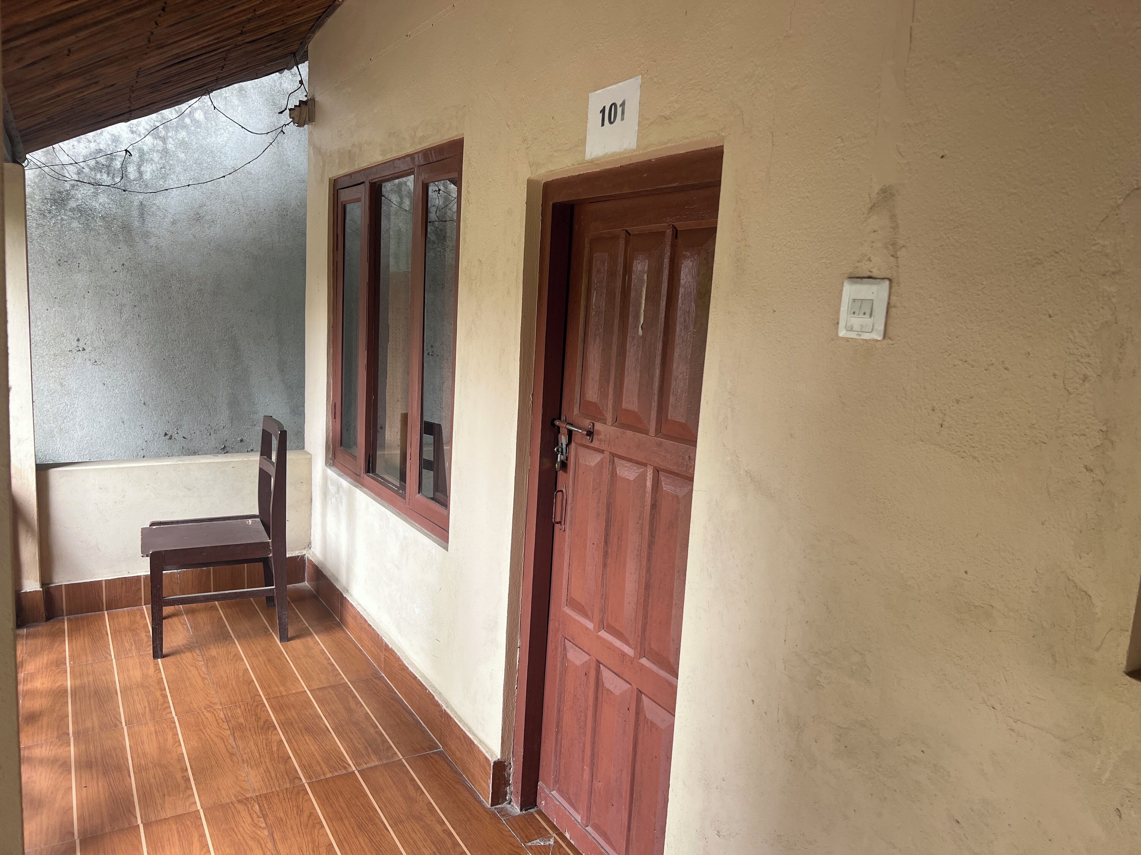 Un pasillo con una puerta de madera marcada '101', una silla y un piso de baldosas.
