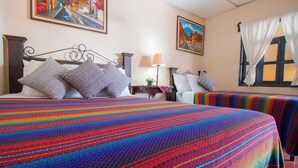 Camera d'albergo con due letti, coperte a righe colorate, un comodino con una lampada e opere d'arte alle pareti.