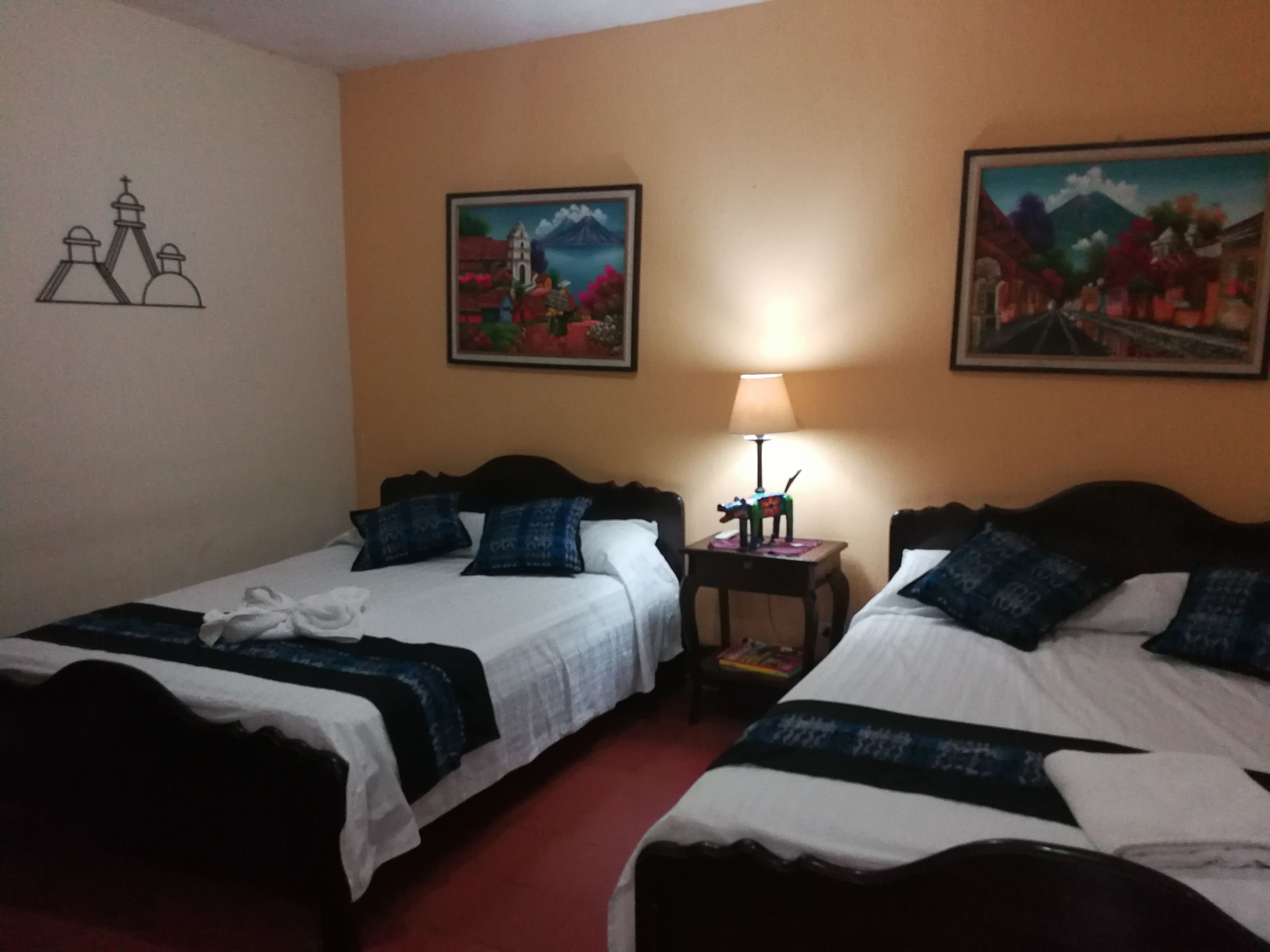Ein Hotelzimmer mit zwei Betten, einem Nachttisch mit Lampe und zwei Bildern an den Wänden.