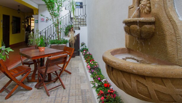 Un cortile con una fontana in pietra, tavolo e sedie di legno, piante in vaso e una scala.