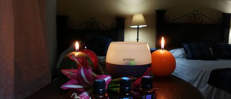 A hotel room with a bed, a nightstand with a lamp, a painting on the wall, and three bottles of DO TERRA essential oils.